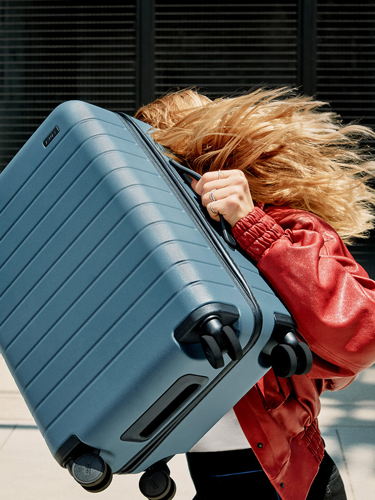 Person in a red jacket holding a blue suitcase with a blurred background