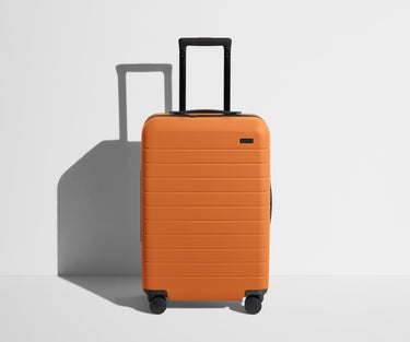 Front product view of The Bigger Carry-On suitcase in Sorbet Orange with raised handle