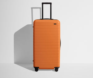 Front product view of The Trunk suitcase in Sorbet Orange with raised handle