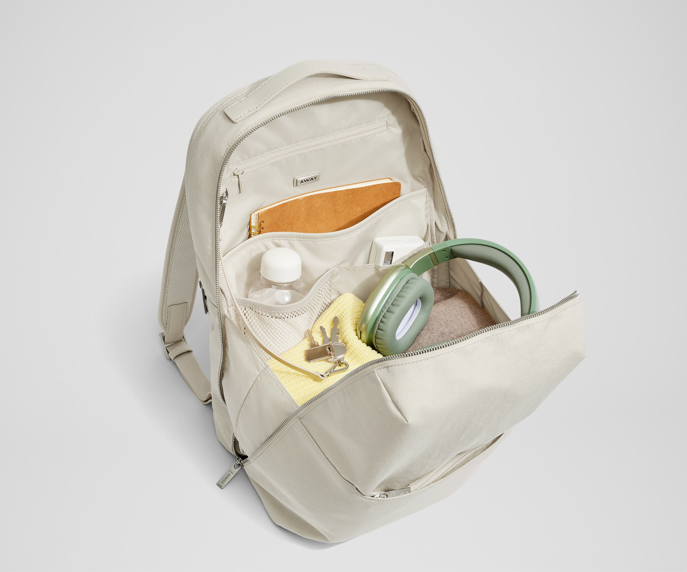 Courtside Everywhere Zip Backpack main compartment packed with a notebook, water bottle, headphones, and sweaters. Keys are attached to interior key leash.