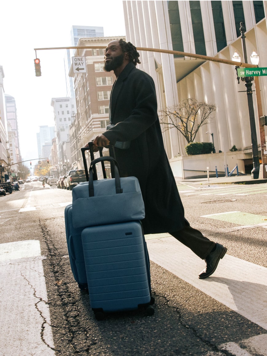 A man exploring the streets of Portland with The Carry-On, The Everywhere Bag, and The Softside Medium -- all in Coast Blue.