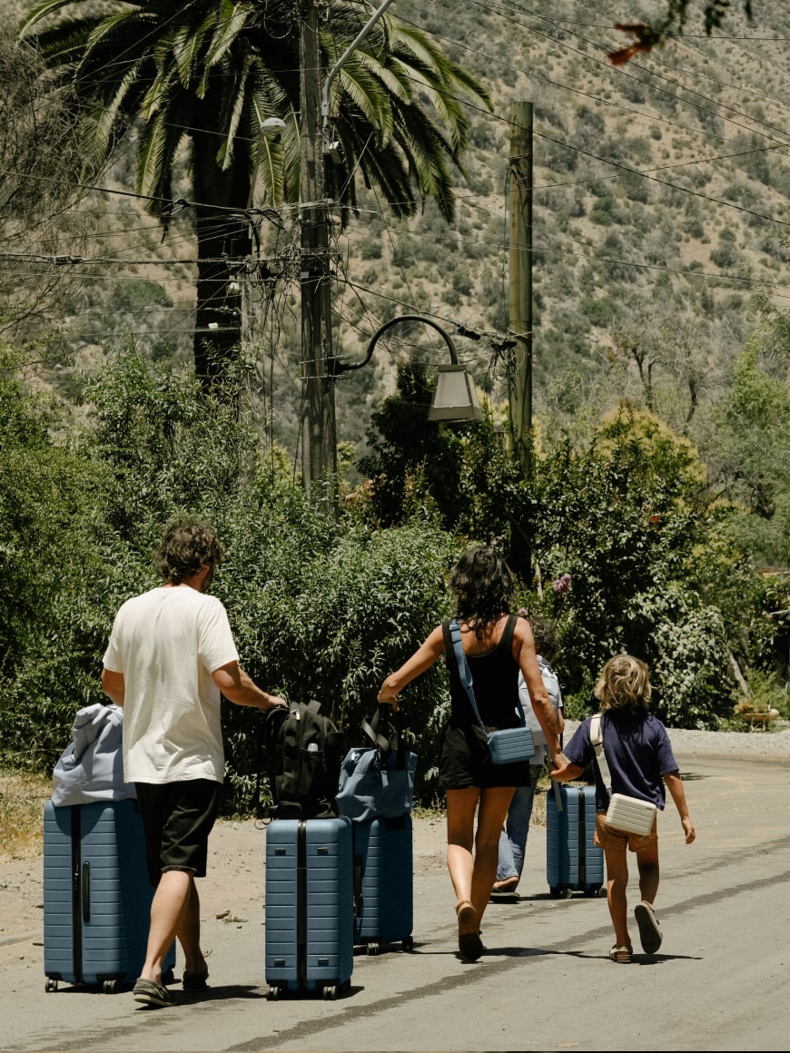 A family of three walking on a lush road with a set of Away suitcases in blue