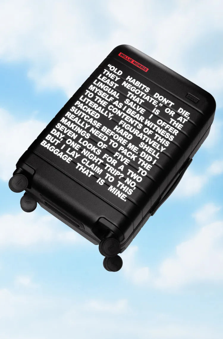 A black Away carry-on suitcase with a Willie Norris quote printed on the front