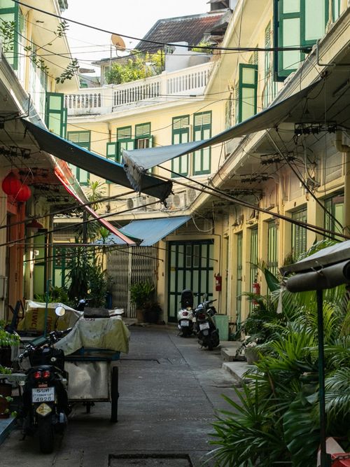 a colorful alleyway in Bangkok with yellow building and green shutters