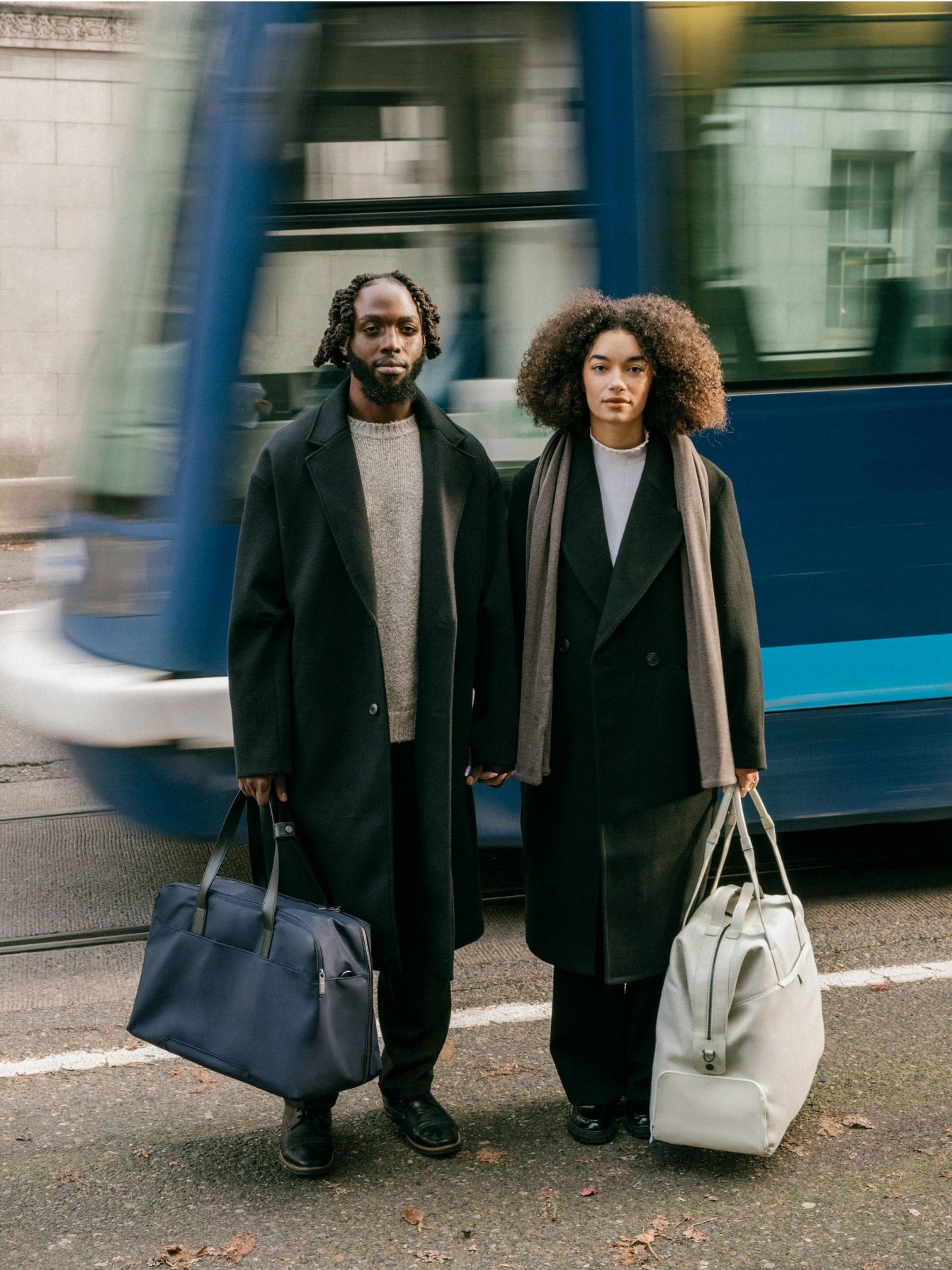 a man an woman standing on the streets of Portland with The Weekender in Navy Blue and The Transit Canvas Weekender in Tan