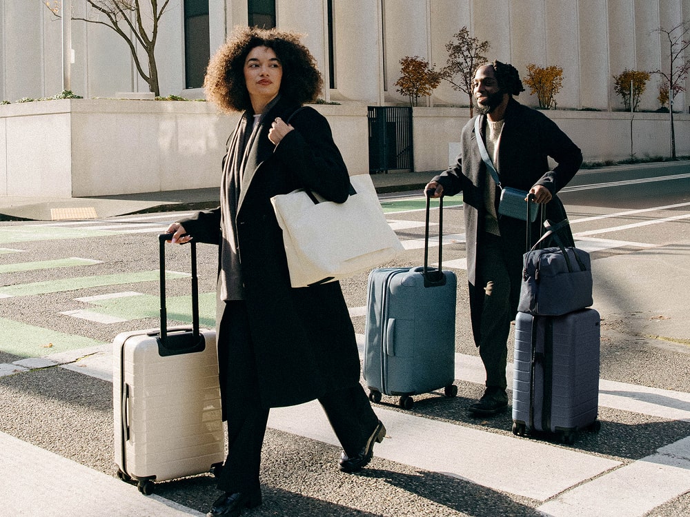 A man and woman crossing the street in Portland, rolling three Away suitcases and holding 3 Away bags