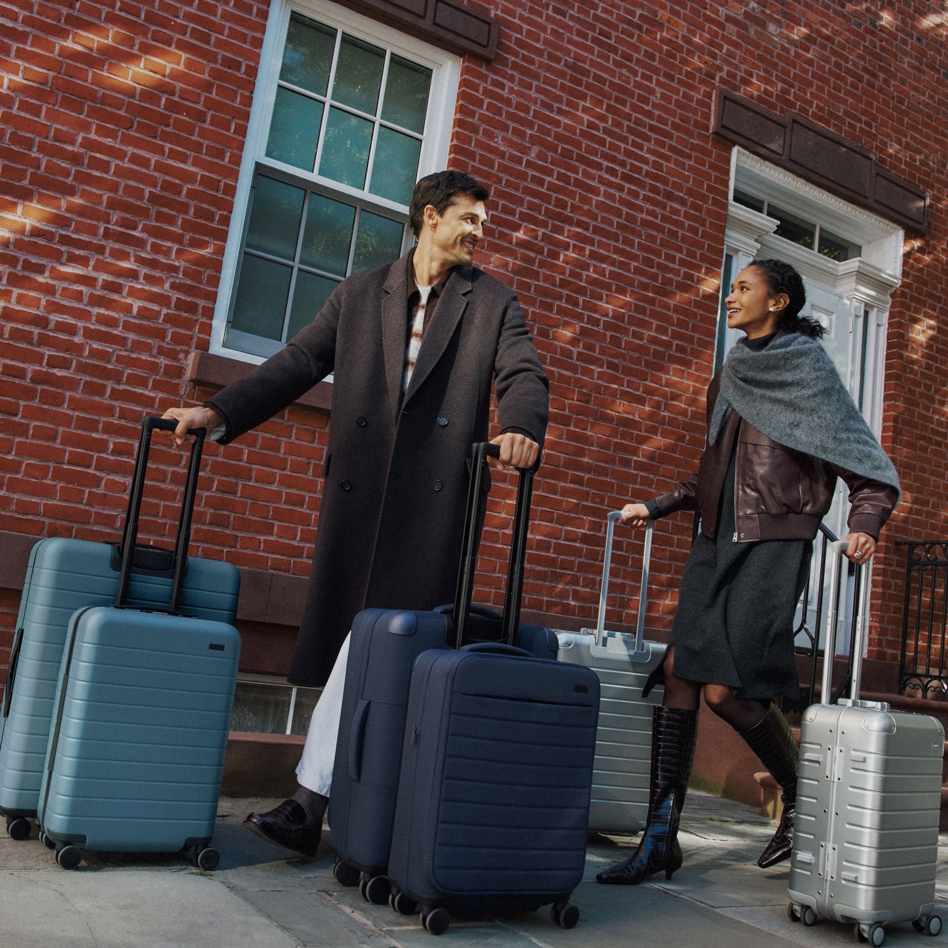 A man an woman in winter rolling 3 sets of Away luggage un blue, navy, and Aluminum silver